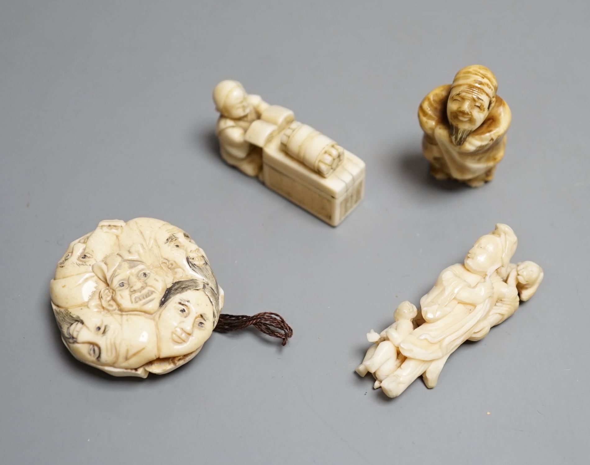 A Japanese ivory netsuke of a man reading a book, a small okimono of Guanyin and monkeys, a Manju netsuke of masks and an early 20th century netsuke of a bearded man